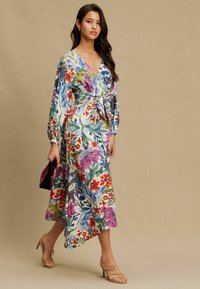 Ziedu raksta apvalka kleita zilā, rozā un zaļā krāsā ar garām piedurknēm un jostu viduklī. Viegls audums ar plūstošu, asimetrisku apakšu.