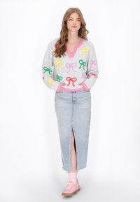 Pulover deschis la culoare, de nuanță gri, cu modele colorate în formă de fundițe, decolteu în V, cu margini roz. Purtați-l cu o fustă din denim cu talie înaltă, având o fanta frontală, asortat cu pantofi roz.