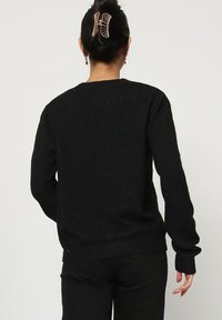 Pull en tricot noir à col rond et manches longues, présentant un tissu texturé et des poignets et un ourlet côtelés. Pas de motifs marquants.