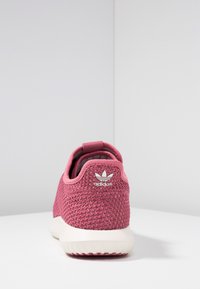 Rosa Adidas-sneakers med en strukturerad mesh-övre, en vit gummisul, och en liten logotyp på hälen. Bakåtsikt visar designens detaljer.