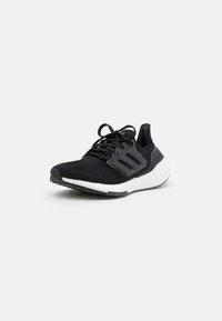 Czarne sportowe sneakersy z białą, wyściełaną podeszwą, czarnymi sznurówkami i czarnym plastikowym wsparciem bocznym, lekko nachylone w lewo na białym tle.