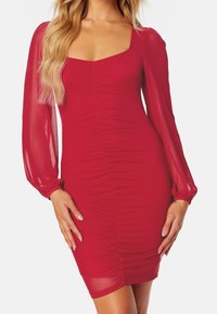 Robe rouge ajustée avec un décolleté carré et des manches bouffantes transparentes. Tissu texturé avec fronces sur les côtés.