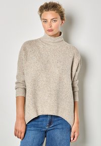 Maglione beige oversize a maglia con collo alto, polsini a coste e finitura testurizzata con schizzi colorati; l'orlo è curvo nella parte inferiore.