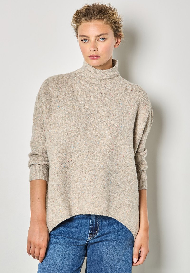 Maglione beige oversize a maglia con collo alto, polsini a coste e finitura testurizzata con schizzi colorati; l'orlo è curvo nella parte inferiore.