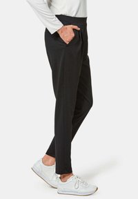 Zwarte broek met een elastische tailleband, zijzakken, taps toelopende benen en een gladde textuur, gecombineerd met witte sneakers.