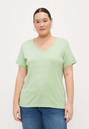 T-shirt vert clair à manches courtes en V, fabriqué en tissu doux et texturé avec un léger éclat, associé à un jean en denim bleu.