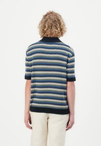 Polo shirt en tricot à manches courtes, avec un motif en zigzag bleu, vert, blanc et noir. Col noir et accents à l'ourlet.