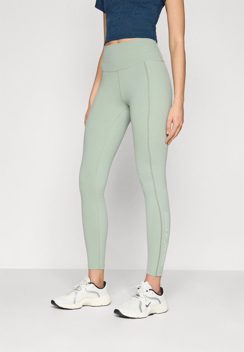 Világoszöld, magas derekú leggings varrással és fehér logó részletekkel, fehér sportcipővel párosítva. Sima, elasztikus anyag.