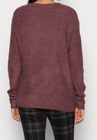 Maglione ribbed bordeaux a vestibilità ampia e maniche lunghe, con collo rotondo e orlo posteriore leggermente più lungo, abbinato a pantaloni a scacchi.