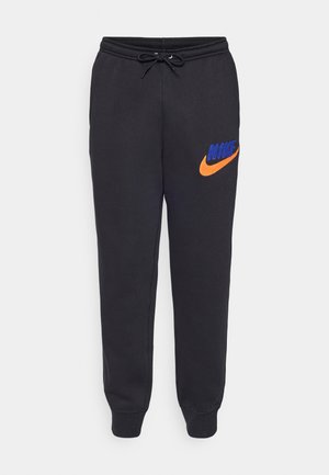 Pantalones de chándal negros con cintura ajustable mediante cordones, que presentan un logo bordado de Nike en naranja y azul en el muslo izquierdo. Tejido suave y ajuste entallado.