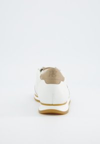 Baskets blanches avec des accents beige, partie supérieure en cuir texturé, détail de logo à l'arrière et semelle en caoutchouc avec un léger talon. Design minimaliste.