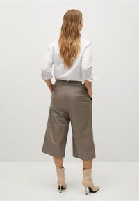 Culottes beige chiaro in tessuto liscio, con tasche laterali. Abbinati a una camicia bianca con bottoni e stivaletti beige.