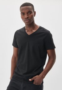 T-shirt nero con scollatura a V, realizzato in morbido tessuto, con maniche corte e silhouette aderente. Texture liscia senza motivi o dettagli visibili.