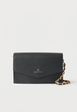 Black textured leather crossbody bag with gold chain strap and gold "Anna Field" logo on front flap.