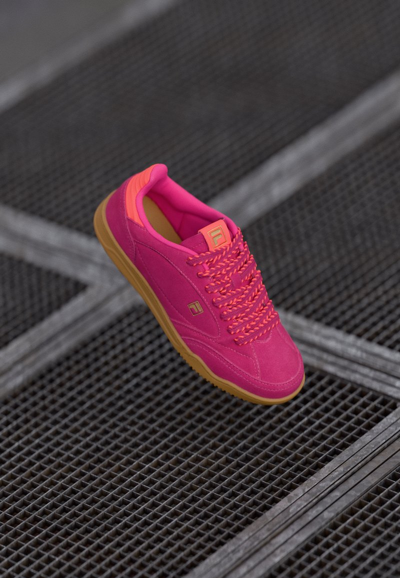 Scarpa atletica rosa con tomaia in suede, dettagli neon e suola in gomma. Presenta una punta tonda e lacci in contrasto.