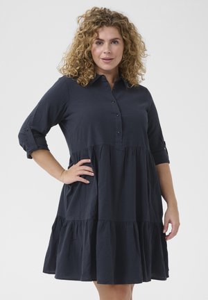 Marineblå kjole med knaplukning foran, trekvartærmer og lagdelt nederdel. Fremstillet af letvægtsstof med en afslappet pasform.