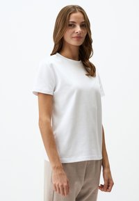 T-shirt bianco in cotone con maniche corte, scollatura rotonda e vestibilità rilassata. Tessuto liscio e dettagli di cucitura sottili all'orlo.