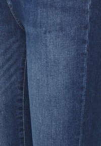 Jeans de ganga azul escuro com uma textura suave, apresentando um corte clássico e um leve desbotado nas costuras. Sem enfeites ou padrões visíveis.