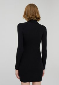 Abito a coste nere a maglia con maniche lunghe, design aderente e colletto alto, che presenta una texture liscia e minimalismo nei dettagli.