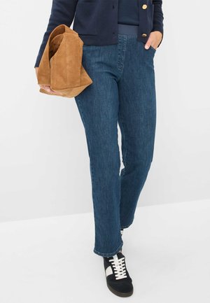 Jeans in denim blu scuro con taglio dritto, abbinati a una borsa in suede marrone e sneakers nere con dettagli bianchi.