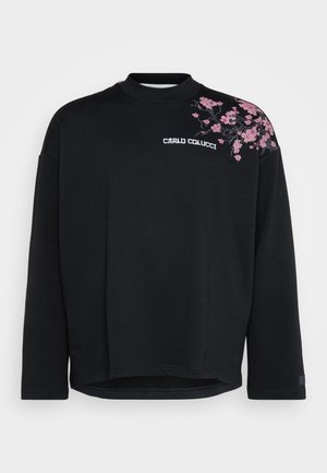 Sudadera negra con cuello alto, que presenta bordado floral rosa en el hombro izquierdo y un logo en el frente. Tejido de textura suave.
