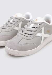 Zapatillas grises con una combinación de ante y material sintético. Presentan cordones blancos, un diseño de cruz blanca y acentos grises texturizados.