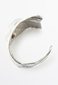 Bracciale a fascia in argento con un design ondulato, caratterizzato da una superficie testurizzata e bordi lucidi. Aperto alle estremità per una vestibilità regolabile.