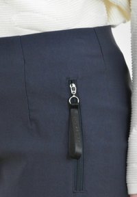 Marineblauwe broek heeft een zijrits met een zwarte stoffen trekband. De stof heeft een gladde textuur en is aansluitend op de taille.