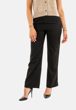 Pantalons larges noirs avec une coupe ajustée, confectionnés dans un tissu lisse. Assortis à des chaussures à talons hauts noires et un cardigan en tricot beige.