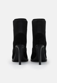 Botines negros con una mezcla de ante y textil, con una parte superior de punto ajustada, puntera afilada y un alto tacón de aguja.