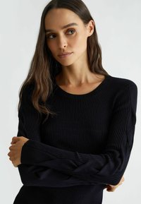 Maglione nero a costine con scollo rotondo e maniche lunghe, caratterizzato da un tessuto testurizzato e una silhouette aderente.