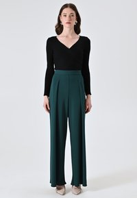 Zwarte geribbelde lange mouwen top met een v-hals, gecombineerd met groene high-waisted wijde broek. Glad materiaal en geplooide details zichtbaar.