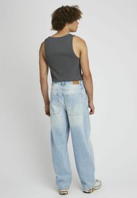 Débardeur gris à côtes associé à un jean en denim bleu clair, ample, avec une teinte délavée et des poches arrière, visibles de l'arrière.