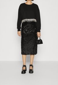 Sweat-shirt noir avec des détails en franges à l'ourlet, assorti à une jupe midi noire en sequins et des chaussures à talons épais noires. Petit sac à main noir.