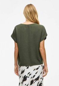 Haut olive, à manches courtes avec une coupe ample et un tissu texturé ; il présente un col large et un ourlet plat, associé à une jupe à motifs.
