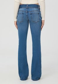 Niebieskie dżinsowe jeansy typu dzwony z średnim stanem, mające dwie tylne kieszenie i gładką fakturę, oferujące klasyczny, swobodny wygląd.