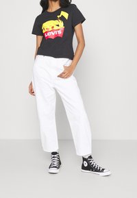 Svart kortärmad T-shirt med en färgglad Pikachu-grafik och "Levi's"-logotyp, kombinerad med vita vida byxor och svarta Converse sneakers.