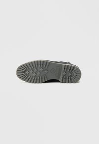 Mustast kummist saapatald, millel on tekstuuriga haardepind, mustriline kulumismuster ja keskel Timberlandi logo.