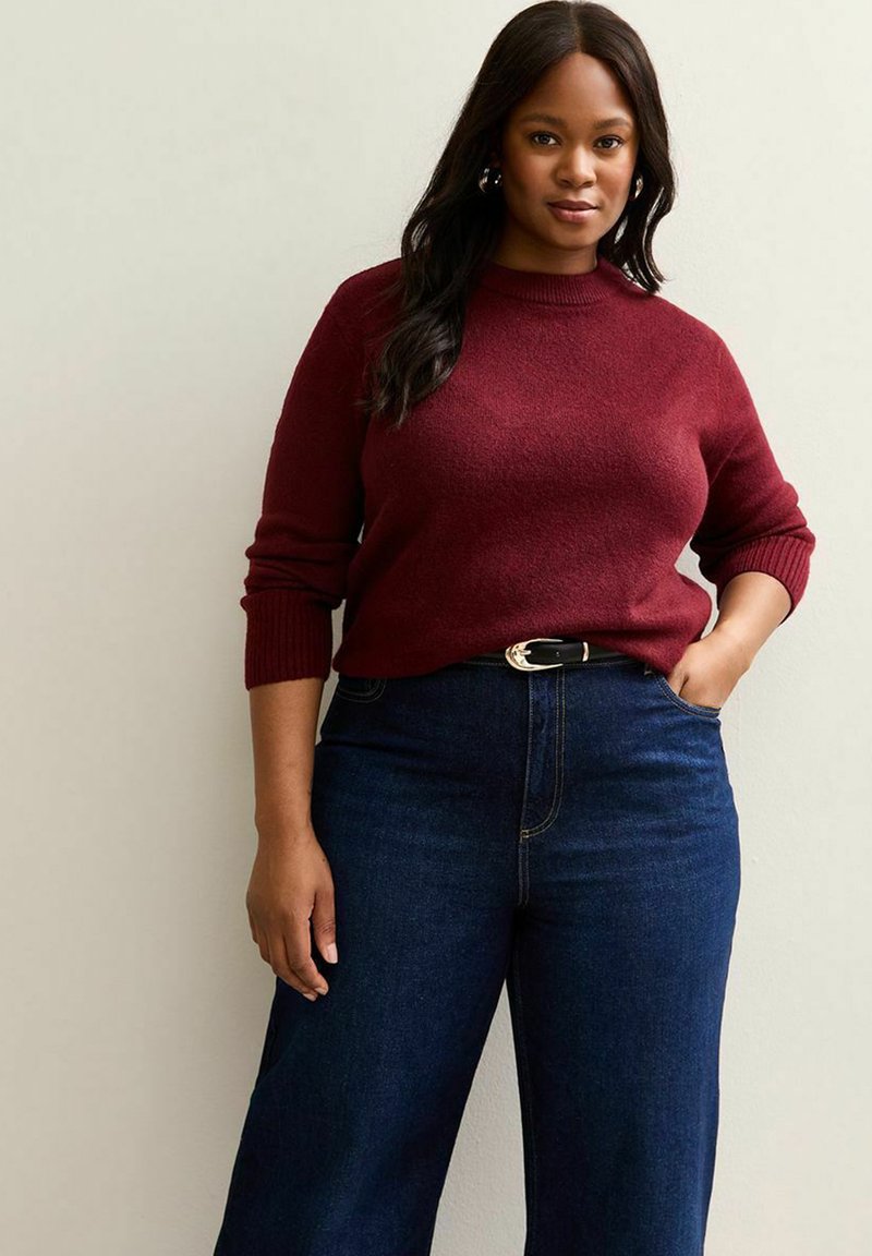 Maglione a maglia bordeaux con collo rotondo e polsini a coste, abbinato a jeans a gamba larga blu scuro a vita alta e una cintura nera con fibbia argentata.