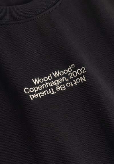 Μαύρο ύφασμα με λευκό κεντημένο κείμενο "Wood Wood Copenhagen, 2002" και "Not to be Trusted" ανάποδα από κάτω.