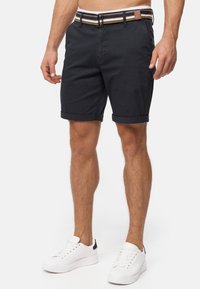 Shorts en coton bleu marine avec ourlets retroussés et une ceinture rayée multicolore. Associés à des baskets blanches avec un accent noir.