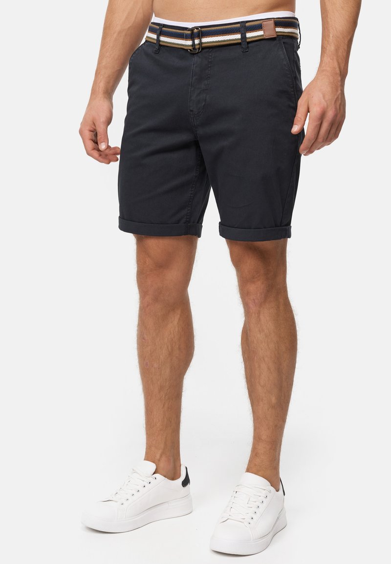 Shorts en coton bleu marine avec ourlets retroussés et une ceinture rayée multicolore. Associés à des baskets blanches avec un accent noir.