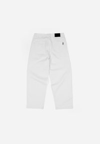 Pantalones de mezclilla blanca con un corte holgado, que presentan un parche negro en la cintura y dos bolsillos traseros. Textura lisa y diseño sencillo.