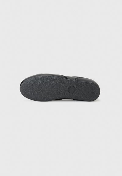 Black shoe bottom with textured rubber sole. Rounded toe, smooth edges, and a circular logo imprint near the heel.