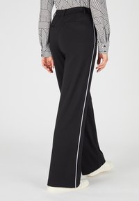 Zwarte wijde broek met een witte zijstreep, gemaakt van een zachte stof. Heeft een tailleband en twee achterzakken.