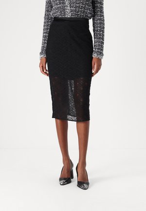 Schwarze Spitzen-Bleistiftrock mit einem Diamantmuster, der eine figurbetonte Silhouette und einen leichten Schlitz aufweist. Kombiniert mit schwarzen High Heels.