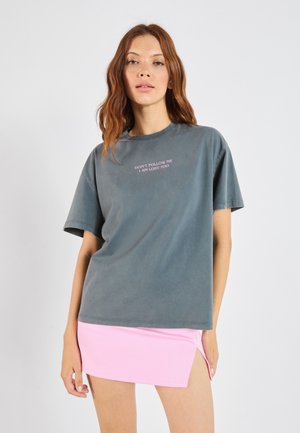 Gray cotton t-shirt with short sleeves and a round neckline, featuring pink text: "DON'T FOLLOW ME I AM LOST TOO." Paired with a pink mini skirt.