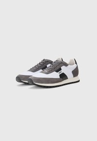Gray and white sneakers featuring suede and mesh materials, with a black accent logo, rounded toe, and textured rubber sole.