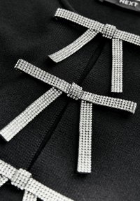 Schwarzer Stoff mit drei dekorativen Schleifen aus Strasssteinen, ausgestattet mit einer strukturierten Oberfläche und glänzenden Akzenten.