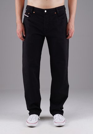 Schwarze Denim-Jeans mit geradem Schnitt, ausgestattet mit Kupferriegeln, Vordertaschen und einem Knopfverschluss. Getragen mit weißen Turnschuhen.